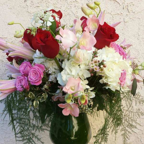 Mixed bouquet of red roses, pink orchids, and white hydrangeas in a glass vase