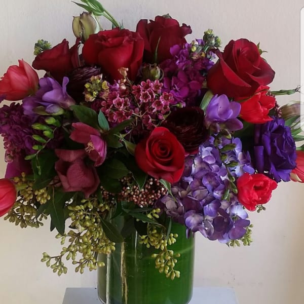 Red roses and purple flowers arranged in a green glass vase