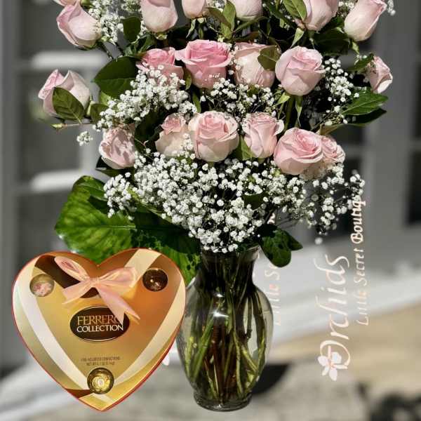 Pink roses in a glass vase with baby's breath and a heart-shaped chocolate box