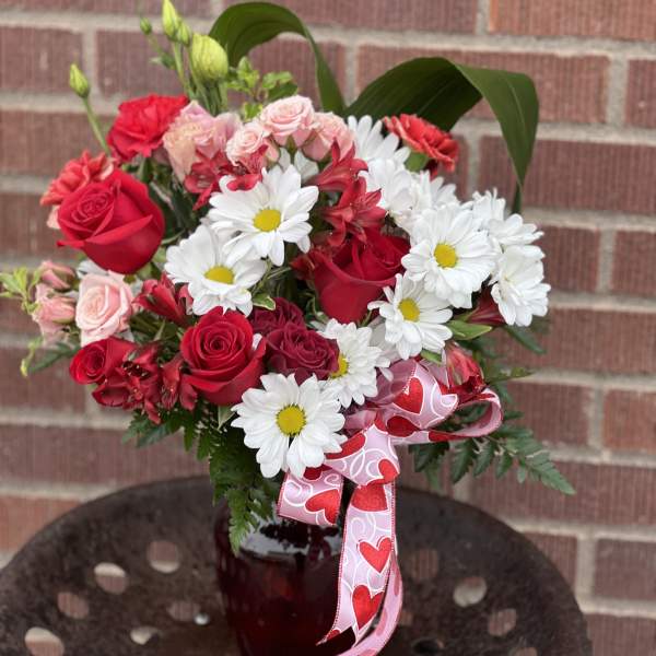 Bouquet of red roses and white daisies in a red vase with a heart ribbon