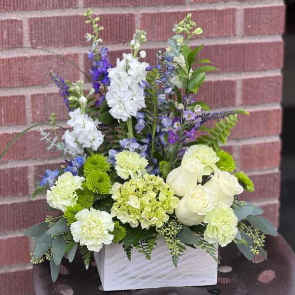 White and green floral arrangement with blue accents in a white container