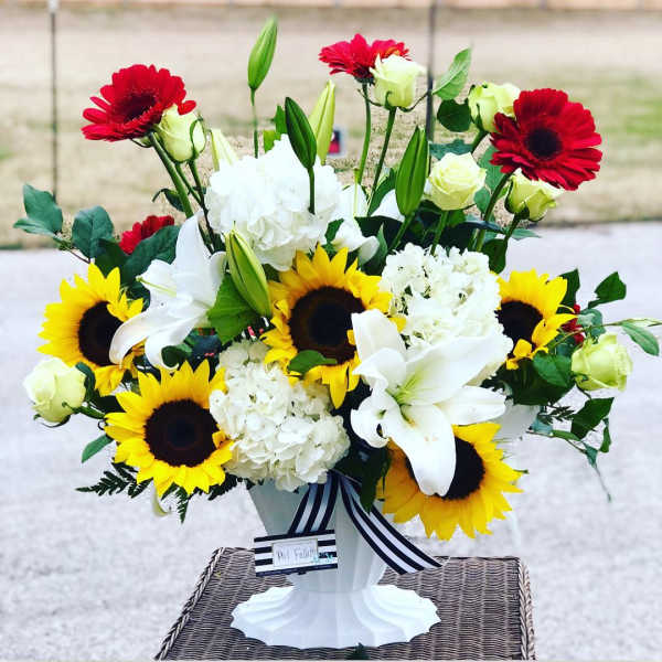 Bouquet of sunflowers, white lilies, and red gerbera daisies in a white vase