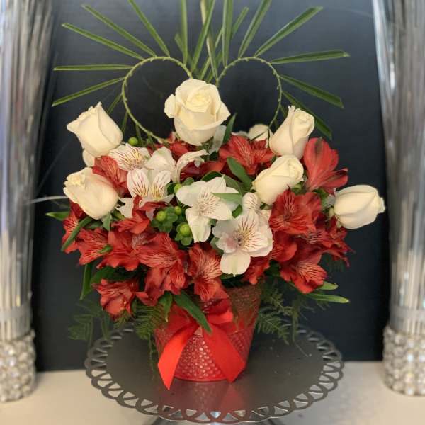 Red and white floral arrangement in a red vase with a ribbon