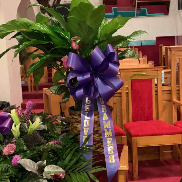 Large green plant arrangement with a purple ribbon in a church pew