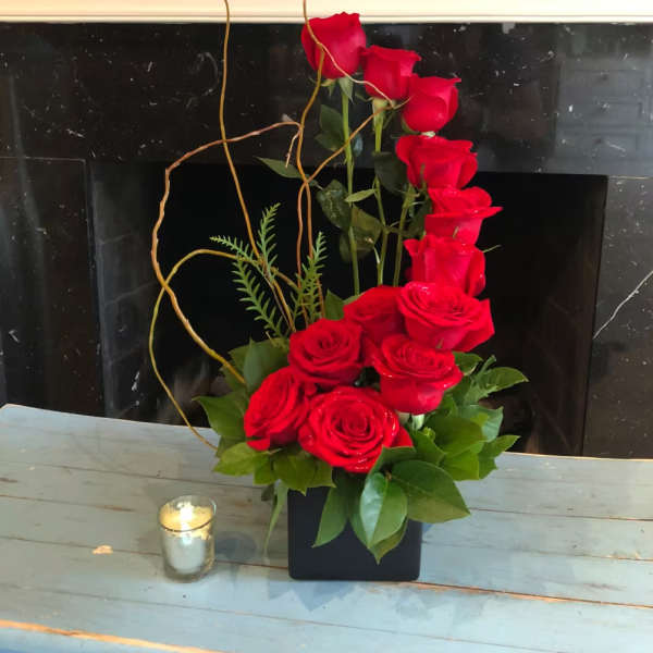 Red roses arranged in a tall black vase with curly branches