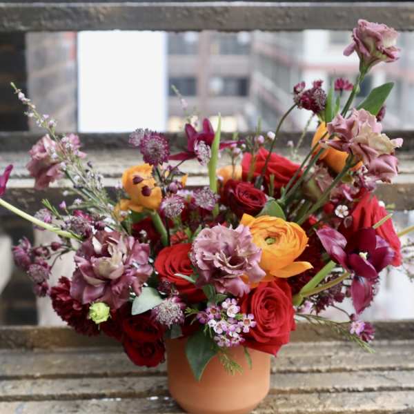 Mixed bouquet of red, pink, and orange flowers in a terracotta vase