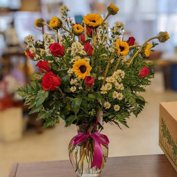 Bouquet of red roses and yellow flowers in a clear glass vase with a pink ribbon