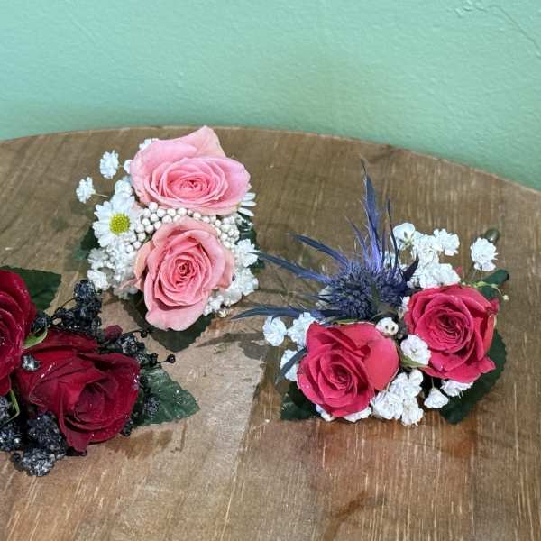 Three small rose corsages with baby's breath on a wooden surface