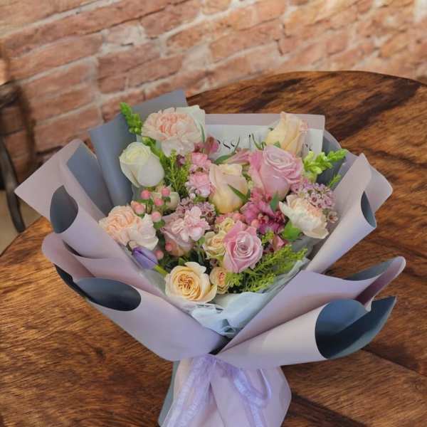 Pastel bouquet of roses and mixed blooms wrapped in lavender paper