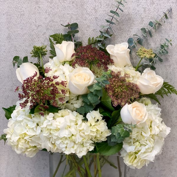 White roses and hydrangeas in a clear glass vase with eucalyptus