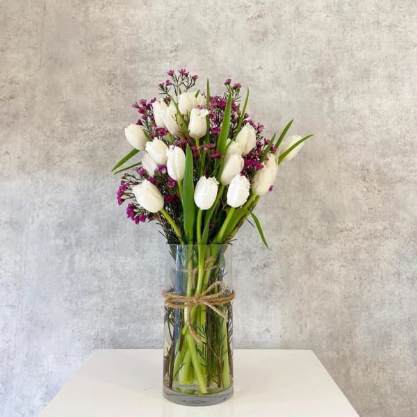 White tulips and purple filler flowers in a clear glass vase
