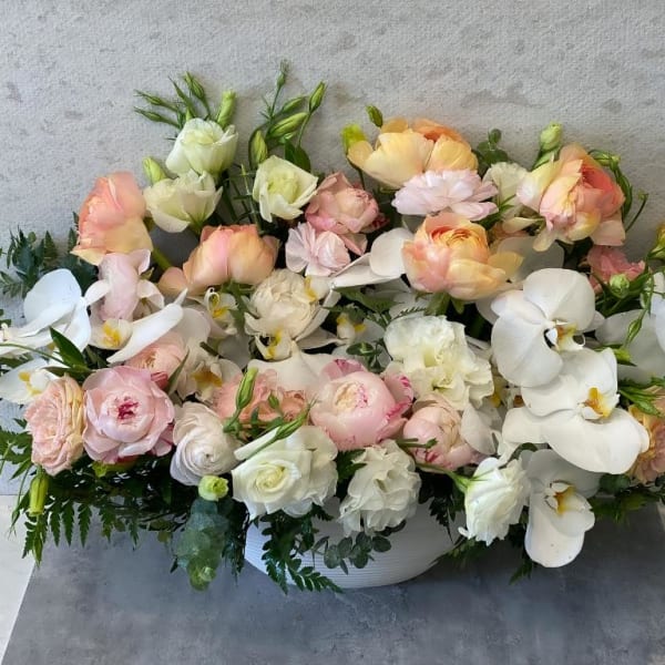 Low floral arrangement of pastel roses and white orchids in a white bowl