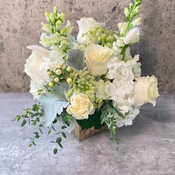White floral arrangement in a square vase with roses and hydrangeas