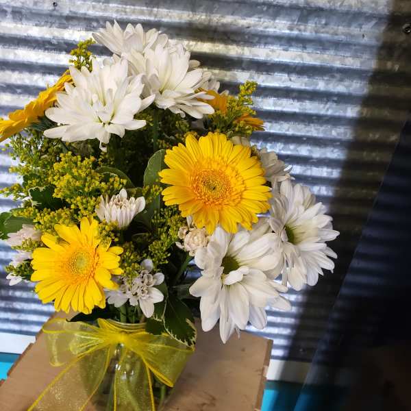 Yellow and white daisy bouquet in a glass jar with a yellow ribbon