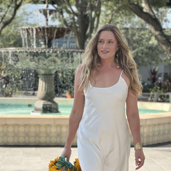 Woman in a white dress holding a wicker basket of sunflowers