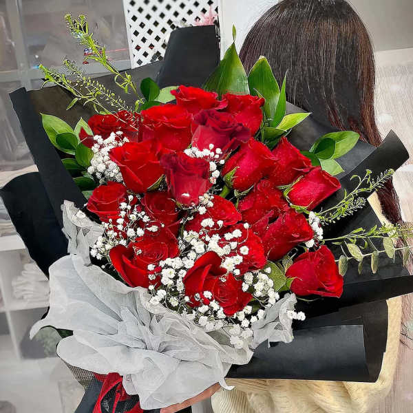 Large hand-tied bouquet of red roses with white filler flowers wrapped in black paper and white tissue.