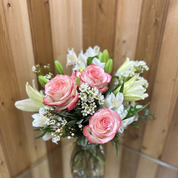Pink roses and white lilies with small white blossoms arranged in a clear glass vase.