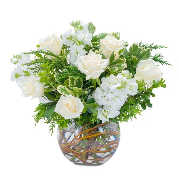 Low arrangement of white roses and stock in a clear glass bowl vase with curly branches in the water