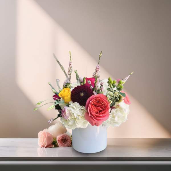 Mixed bouquet of pink, white, and yellow flowers in a white vase