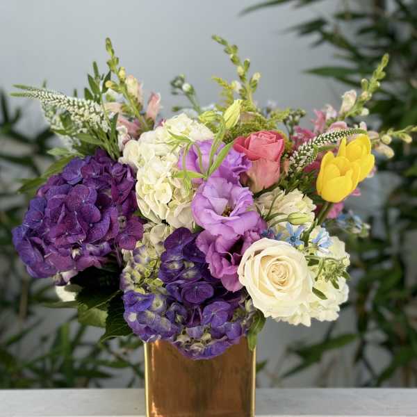 Colorful bouquet in a gold vase with purple hydrangeas, roses, and yellow tulips