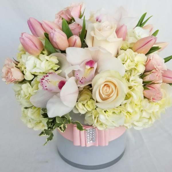 Pink tulips, white roses, and orchids arranged in a round hatbox