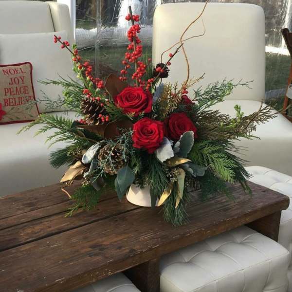 Red roses and berries in a white vase with pinecones and evergreen branches