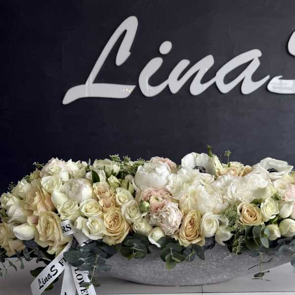 Long low arrangement of cream and blush roses in a silver bowl