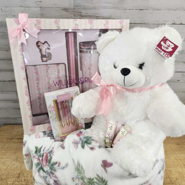 White teddy bear with a pink ribbon beside a floral gift set