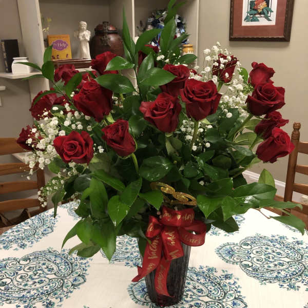 Red roses arranged in a tall black vase with baby's breath and a red ribbon