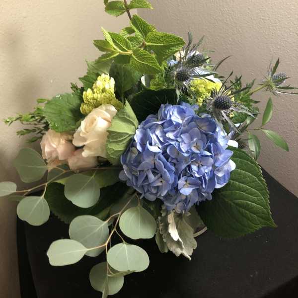 Bouquet of blue hydrangea, pale roses, and thistle in a vase