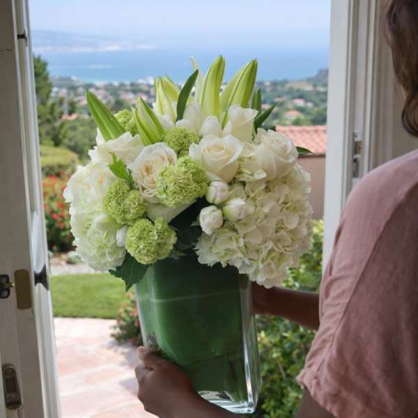 White floral arrangement in a clear glass vase being held at a doorway