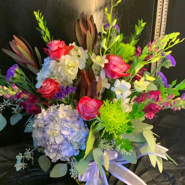 Colorful bouquet of roses, hydrangeas, and orchids with a ribbon bow