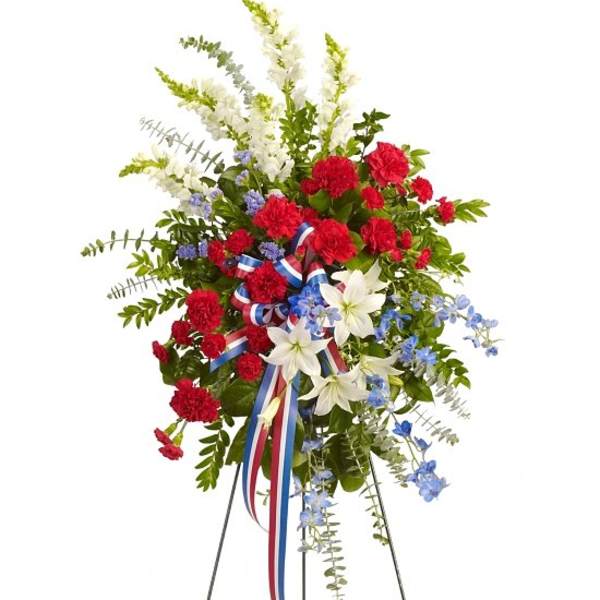 Standing floral spray with red carnations, white lilies, and blue accents on an easel
