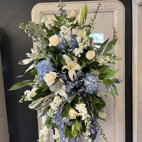 Tall floral spray with blue hydrangeas, white lilies, and cream roses on an easel