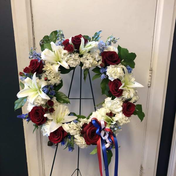 Circular wreath of red roses, white lilies, and white hydrangeas on a stand