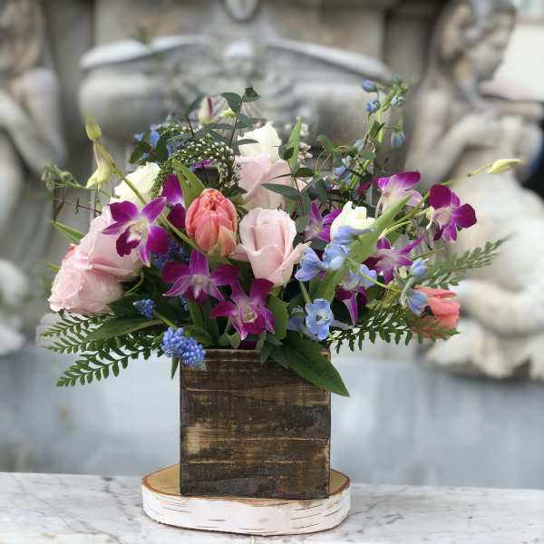 Rustic wood box arrangement with pink roses, tulips, purple orchids, and blue blooms