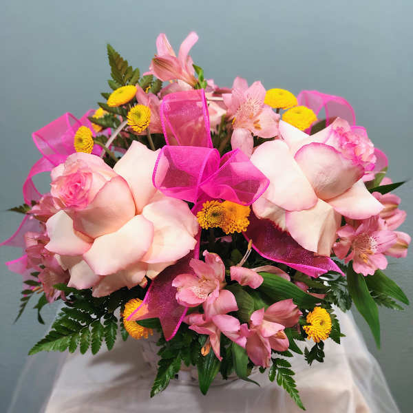 Pink and yellow mixed flower arrangement with roses and alstroemeria in a white basket with bright pink ribbon bows