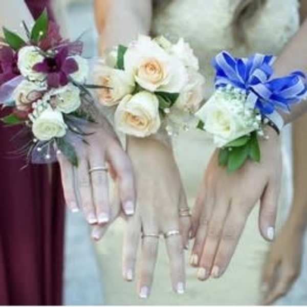 Three floral wrist corsages on women’s hands, in purple, white, and blue.