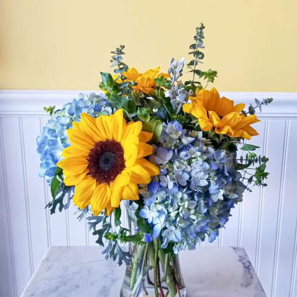 Sunflowers and blue hydrangeas arranged in a clear glass vase