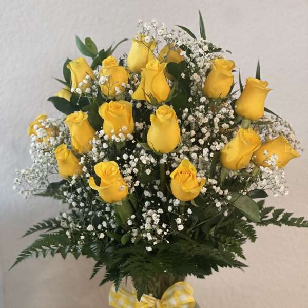 Yellow roses in a clear glass vase with white baby's breath and a gingham ribbon