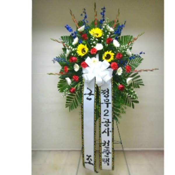 Tall standing spray with yellow sunflowers, red carnations, and white flowers on an easel