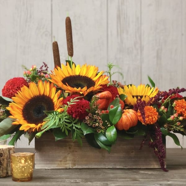 Autumn floral arrangement with sunflowers, red blooms, and pumpkins in a wooden box