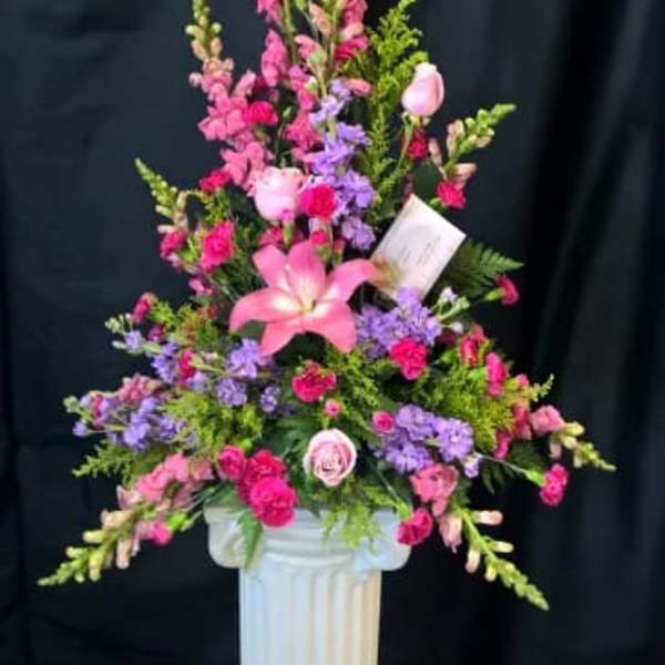 Tall pink and purple floral arrangement in a white pedestal vase