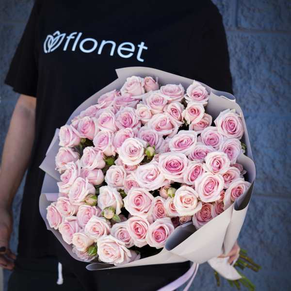 Person holding a large bouquet of pale pink roses wrapped in paper