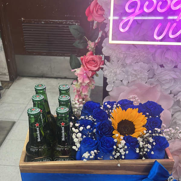 Blue roses and a sunflower in a wooden box with beer bottles
