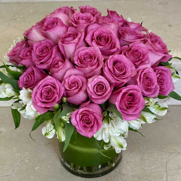 Pink roses arranged in a clear glass vase with white flowers around the base