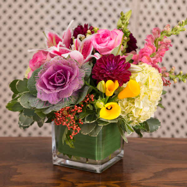 Colorful bouquet in a square glass vase with roses, lilies, and calla lilies