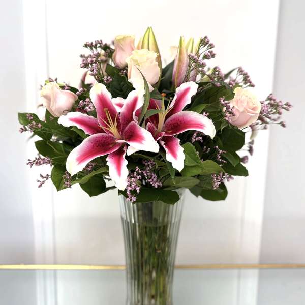 Pink lilies and pale roses in a tall glass vase