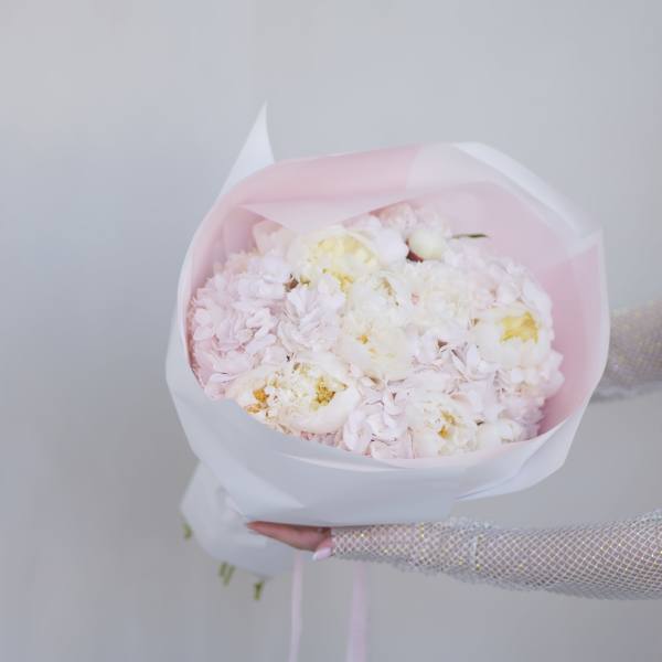 Handheld bouquet of pale pink and white flowers wrapped in pink paper