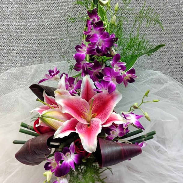 Asymmetrical pink lily and purple orchid arrangement with tall linear accents on sheer fabric